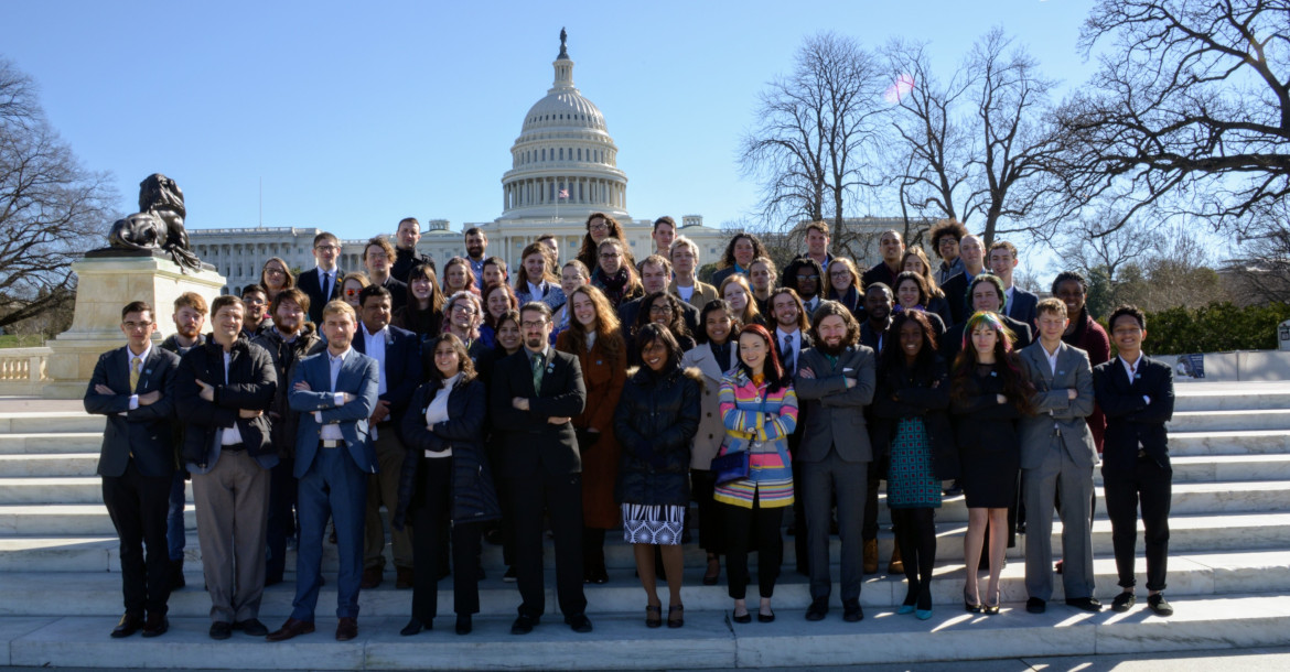 A group of young people in suits with their arms crossed in front of the U.S. Capitol